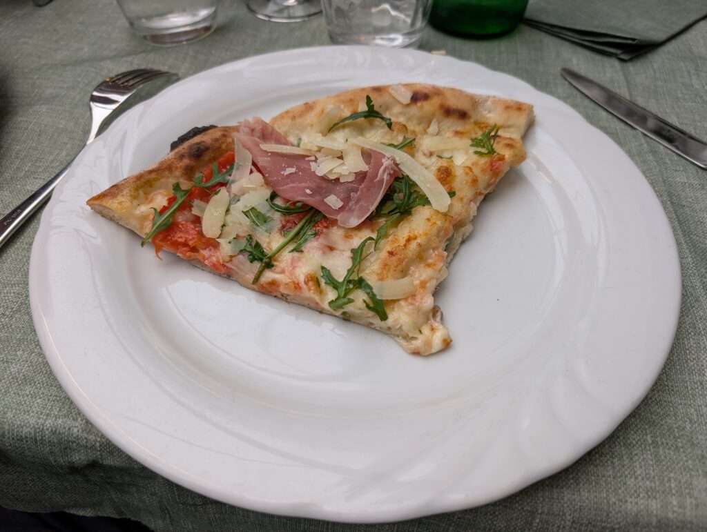 Zbliżenie na kawałek pizzy z szynką parmeńską i rukolą na talerzu w restauracji Pizza a metro da Gigino.