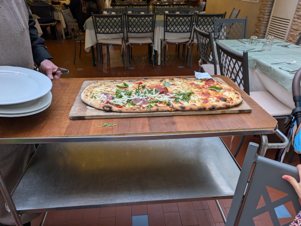 Wielka pizza na metry serwowana na drewnianej desce na wózku kelnerskim w pizzerii Da Gigino.