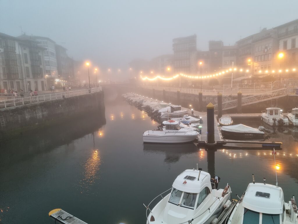 Port w Llanes spowity gęstą mgłą, widoczne zarysy łodzi i świateł