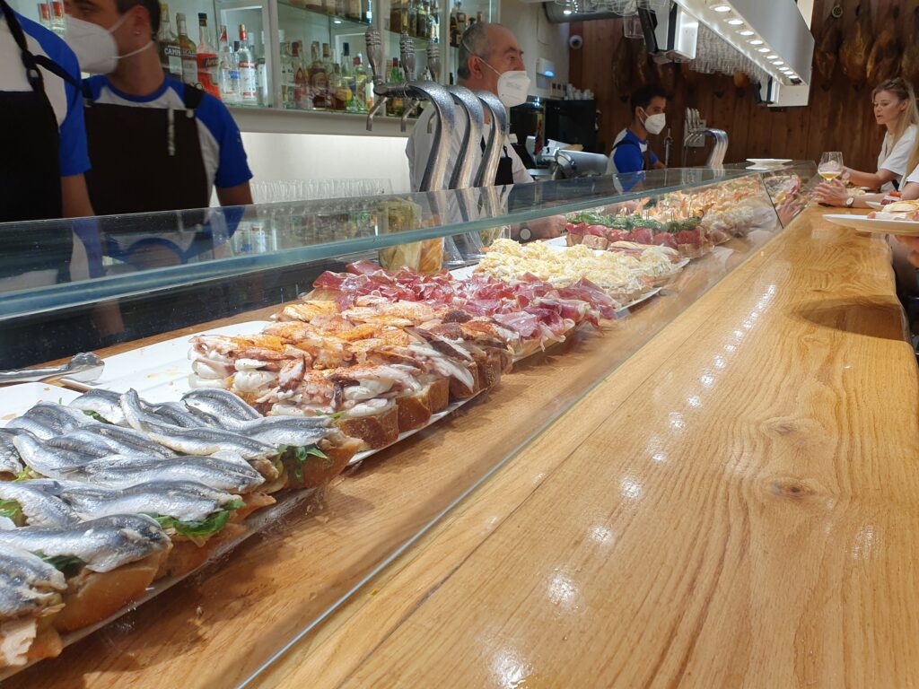 Długa lada barowa zastawiona różnorodnymi przekąskami pintxos w San Sebastian