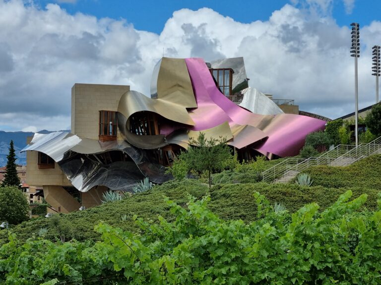 Futurystyczna, tytanowa architektura winnicy Bodegas Marqués de Riscal w La Rioja, zaprojektowana przez Franka Gehry'ego, na tle tradycyjnych zabudowań