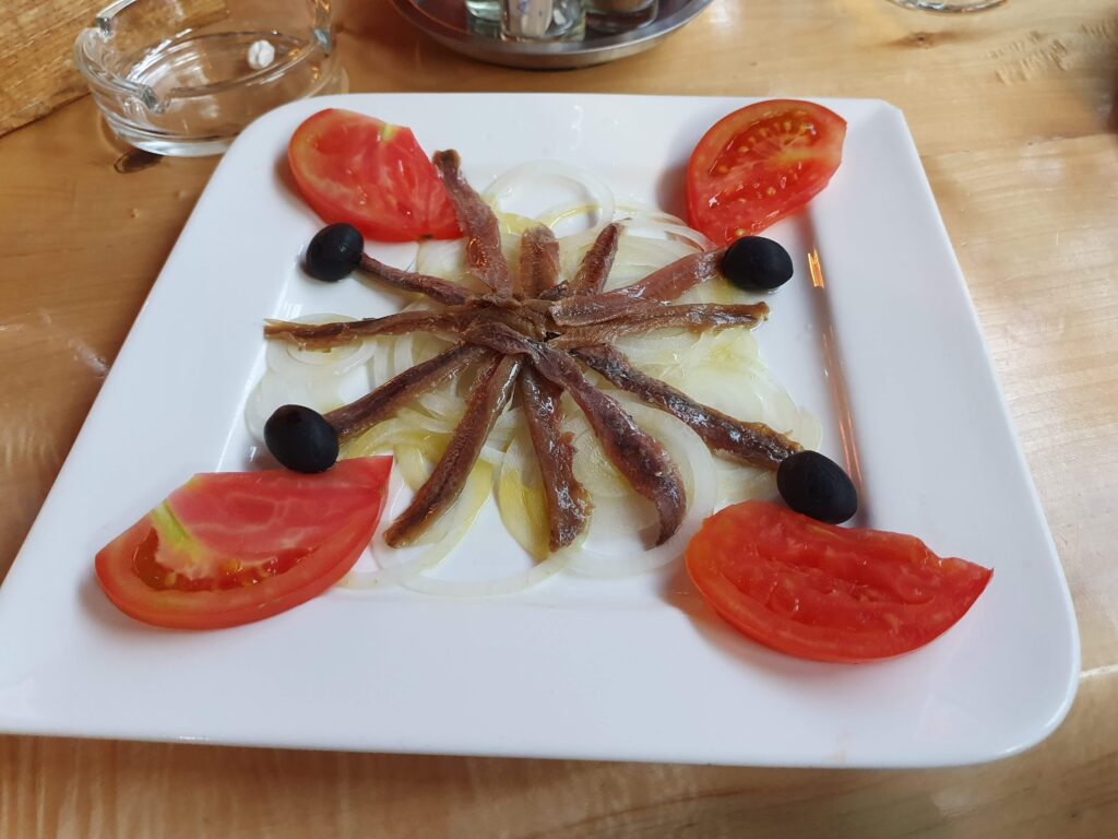 Przystawka z anchois ułożonych w gwiazdę z cebulą, oliwkami i pomidorami