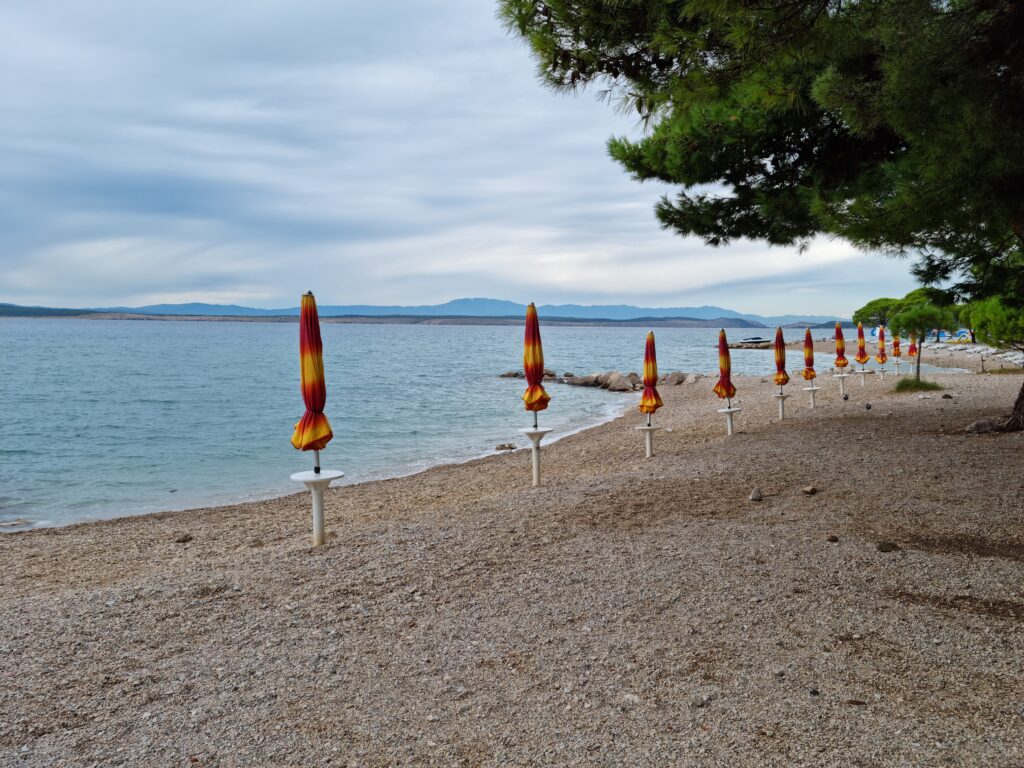 Kolorowe parasole na żwirkowej plaży pod zachmurzonym niebem