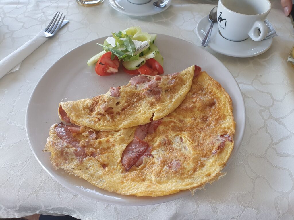 Omlet z bekonem i świeża sałatka podane na białym talerzu