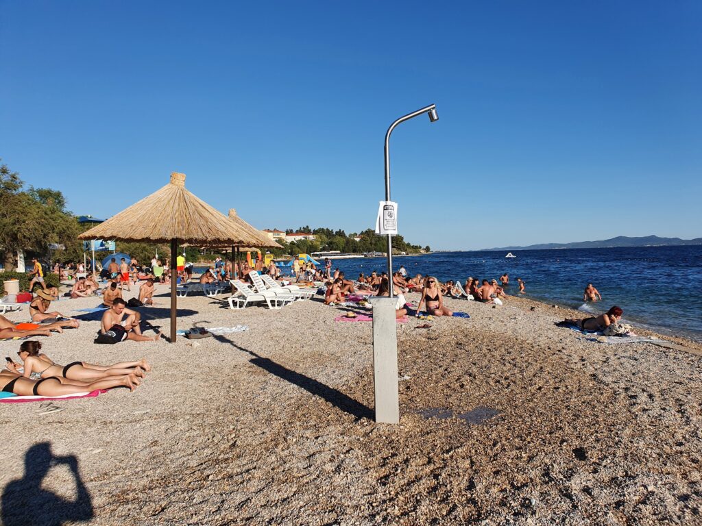 Plaża Kolovare w Zadarze z publicznym prysznicem i rzędami trzcinowych parasoli