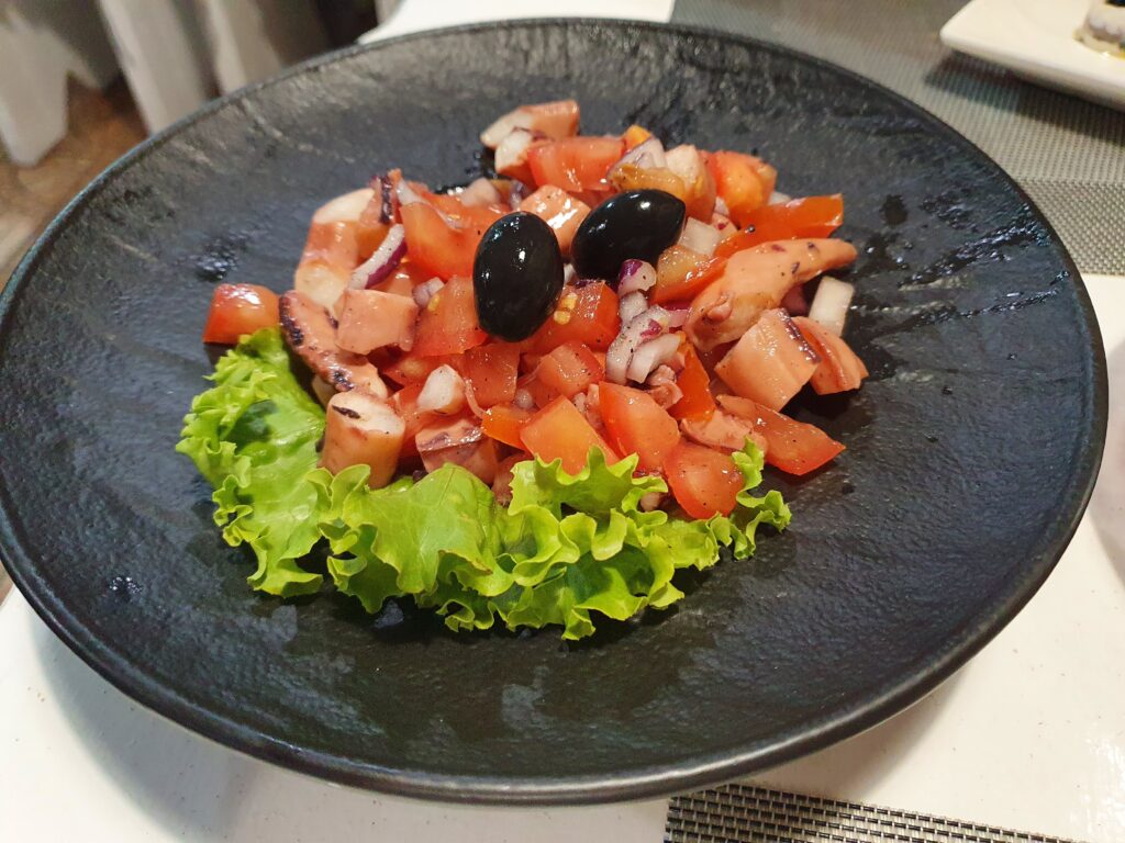 Sałatka z ośmiornicy z pomidorami i czarnymi oliwkami w czarnej misce w Bistro Beppo Cafe.