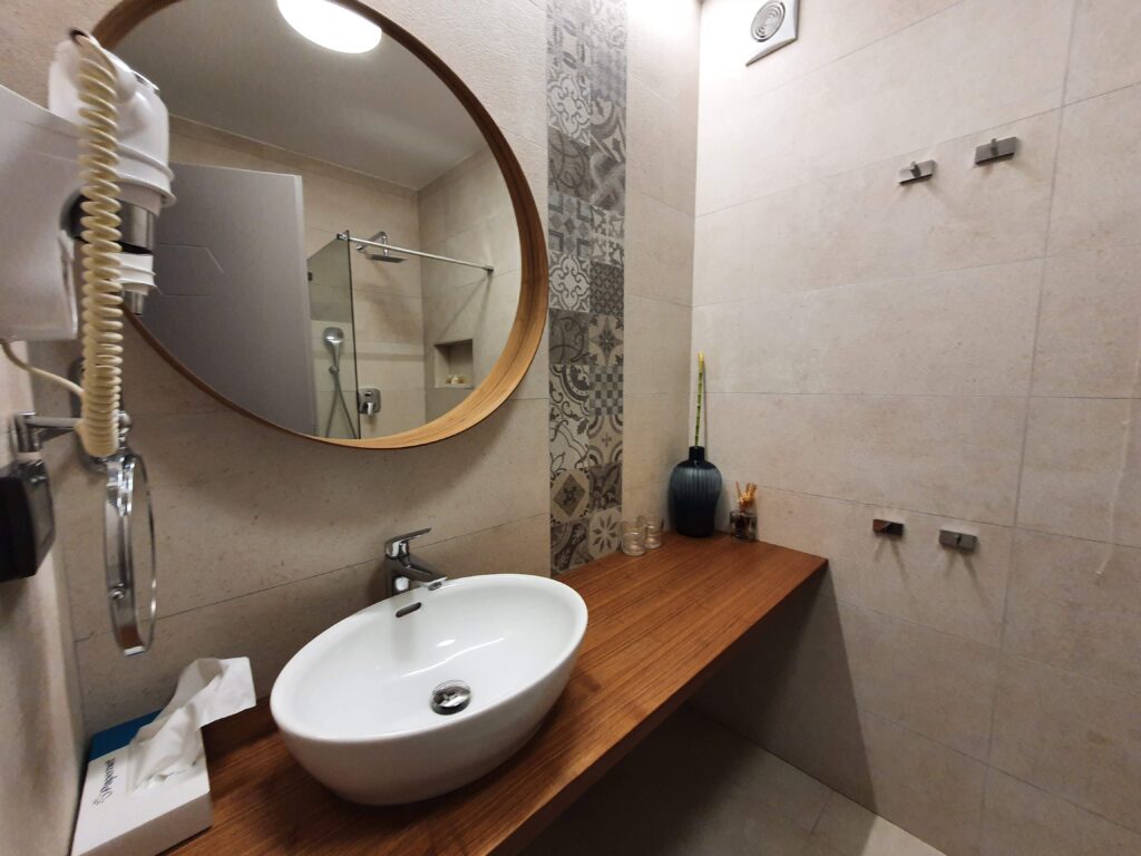 Nowoczesna łazienka z drewnianym blatem i okrągłym lustrem w Hotelu Delfin