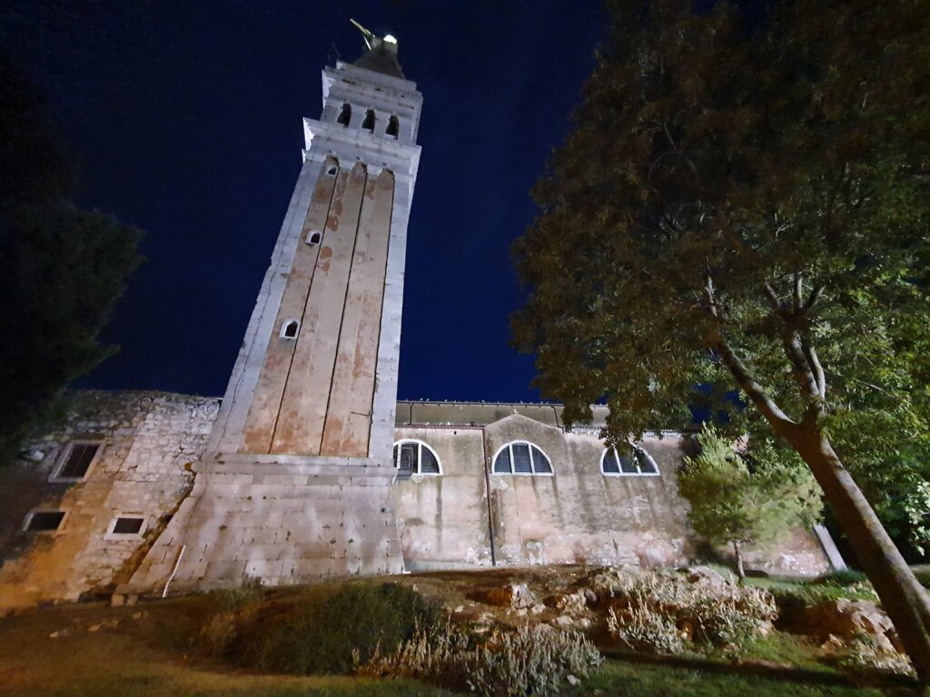 Wysoka, podświetlona dzwonnica kościoła św. Eufemii w Rovinj na tle ciemnego nieba