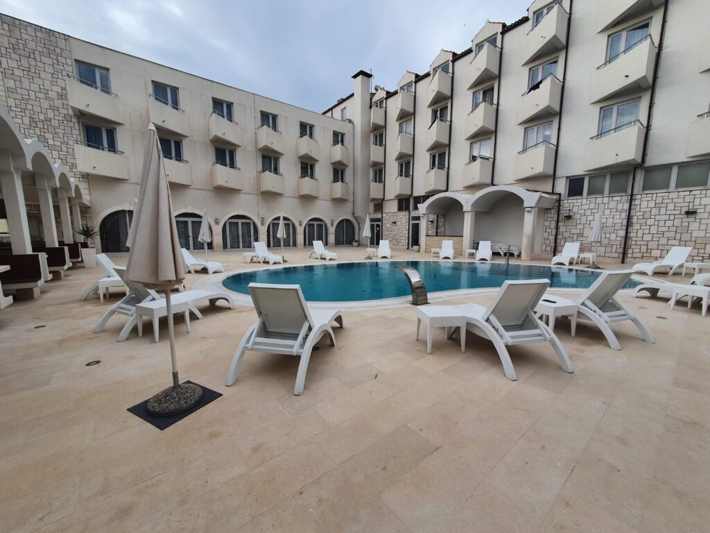 Okrągły basen hotelowy otoczony białymi leżakami na dziedzińcu Hotelu Korkyra.