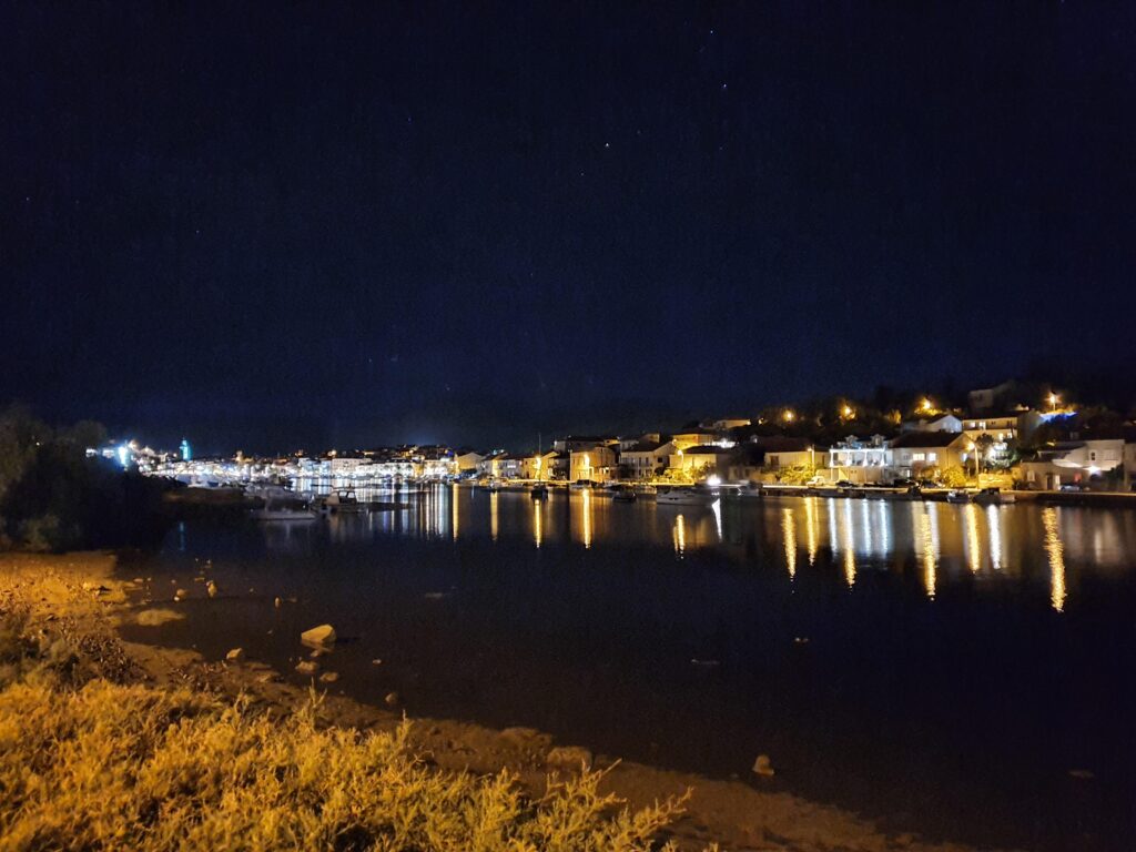 Nocny widok na port w Vela Luka ze światłami odbijającymi się w wodzie zatoki.