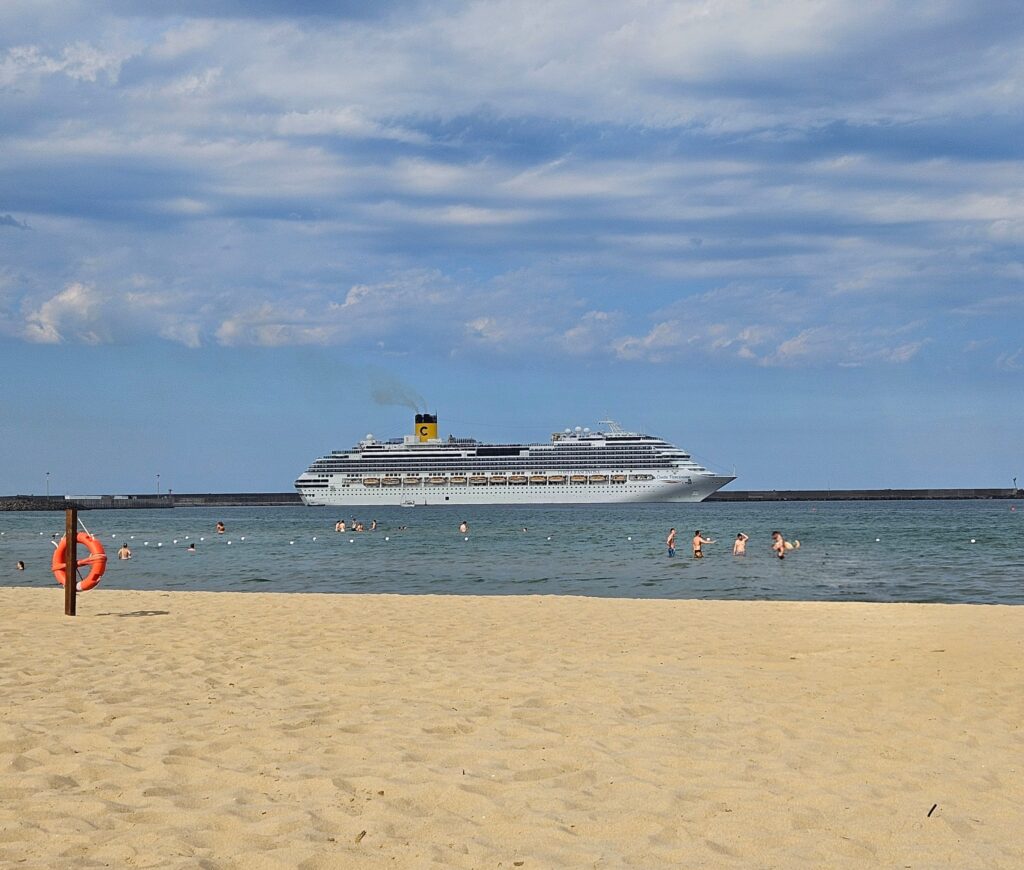 Piaszczysta plaża Lido Azzuro w Katanii z dużym statkiem wycieczkowym widocznym na horyzoncie