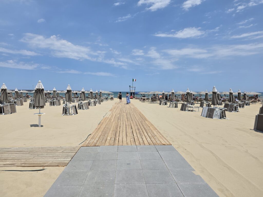 Drewniane kładki prowadzące przez piaszczystą plażę z rozłożonymi leżakami i parasolami