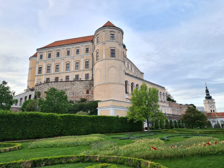 Monumentalny barokowy zamek w Mikulovie wznoszący się nad kamiennym murem porośniętym zielenią.