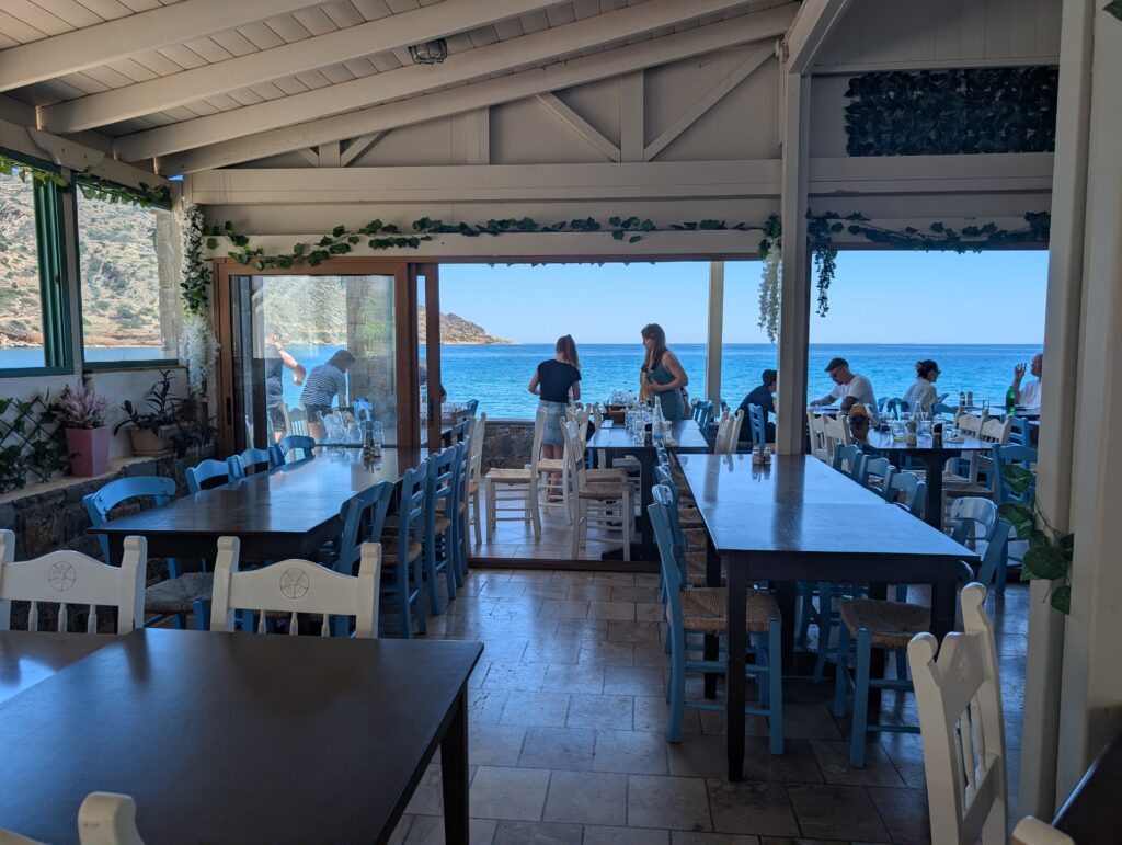 Widok z wnętrza restauracji Taverna Spinalonga przez szeroko otwarte okna na błękitne morze
