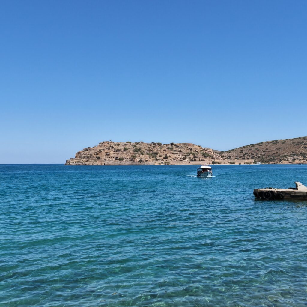 Widok z łodzi na ufortyfikowaną wyspę Spinalonga na Krecie na tle błękitnego nieba